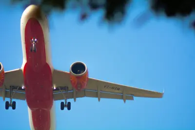 Ett flygplan med landningsställ utfällt syns underifrån mot en blå himmel.