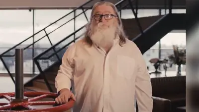Gabe Newell med långt vitt skägg och glasögon står framför en röd ventil. Trappa i bakgrunden.