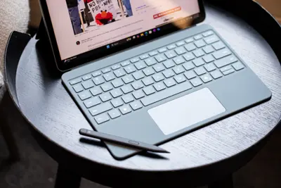 En grå Surface-dator med tangentbord och penna står på ett runt, svart bord. Skärmen visar en webbsida.