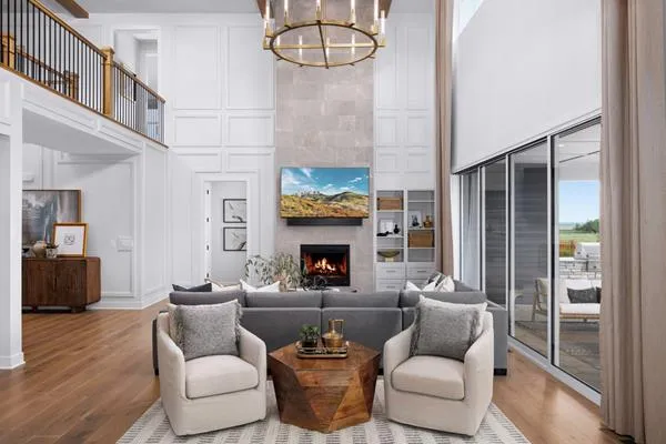 Ett vardagsrum med soffa, fåtöljer, TV över en öppen spis och stora fönster.