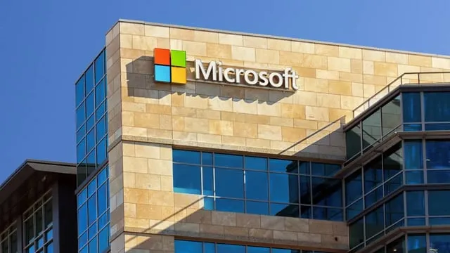 En byggnad med Microsofts logotyp och namn på fasaden. Blå himmel i bakgrunden.