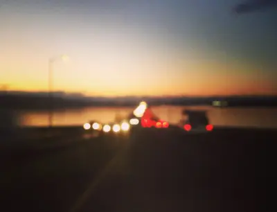 Oskarp bild av en väg med bilar i solnedgången. Vatten syns i bakgrunden.