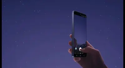 En hand håller en mobiltelefon mot en stjärnklar himmel. Telefonens skärm visar en kameraapp.