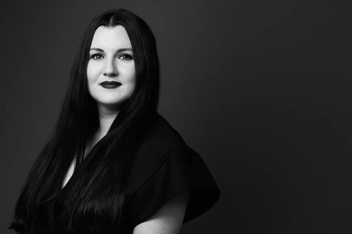 Svartvit porträttbild av kvinna med långt, mörkt hår och mörka läppar. Hon bär en mörk klänning.