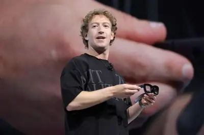 Mark Zuckerberg håller i ett par svarta glasögon på en scen. I bakgrunden syns en stor hand.